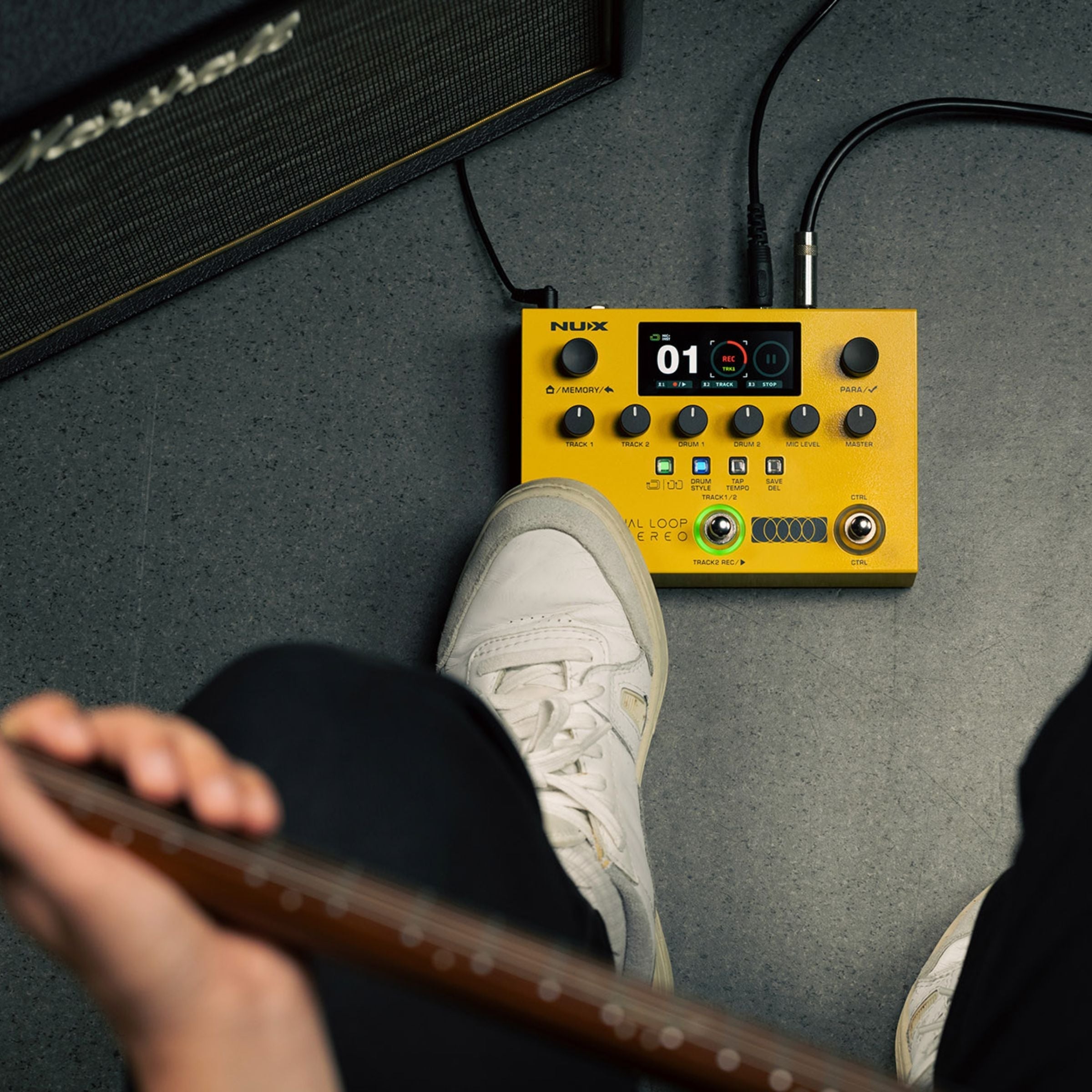 yellow NUX pedal on floor with foot on one of the switch next to an amp